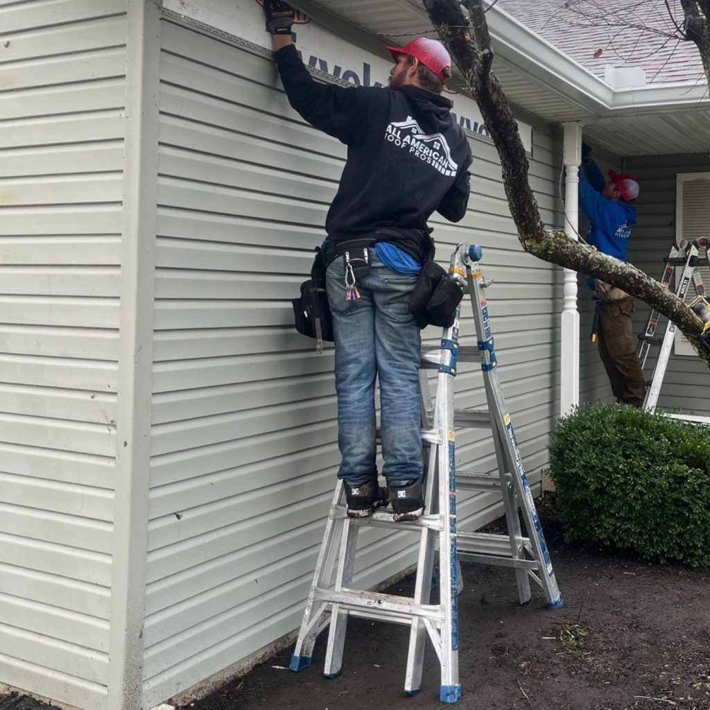 Production team member on a ladder working on the gutters on the side of a house in Ohio